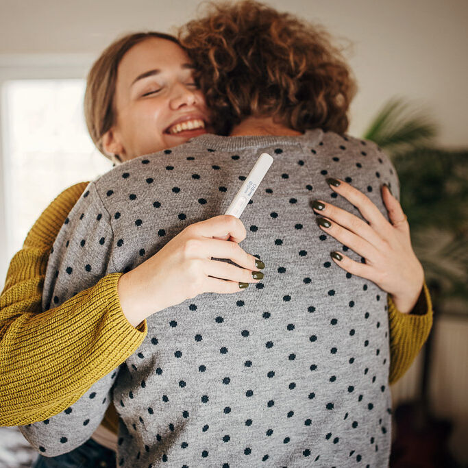 Ein Paar umarmt sich glücklich, sie hält einen Schwangerschaftstest in der Hand.