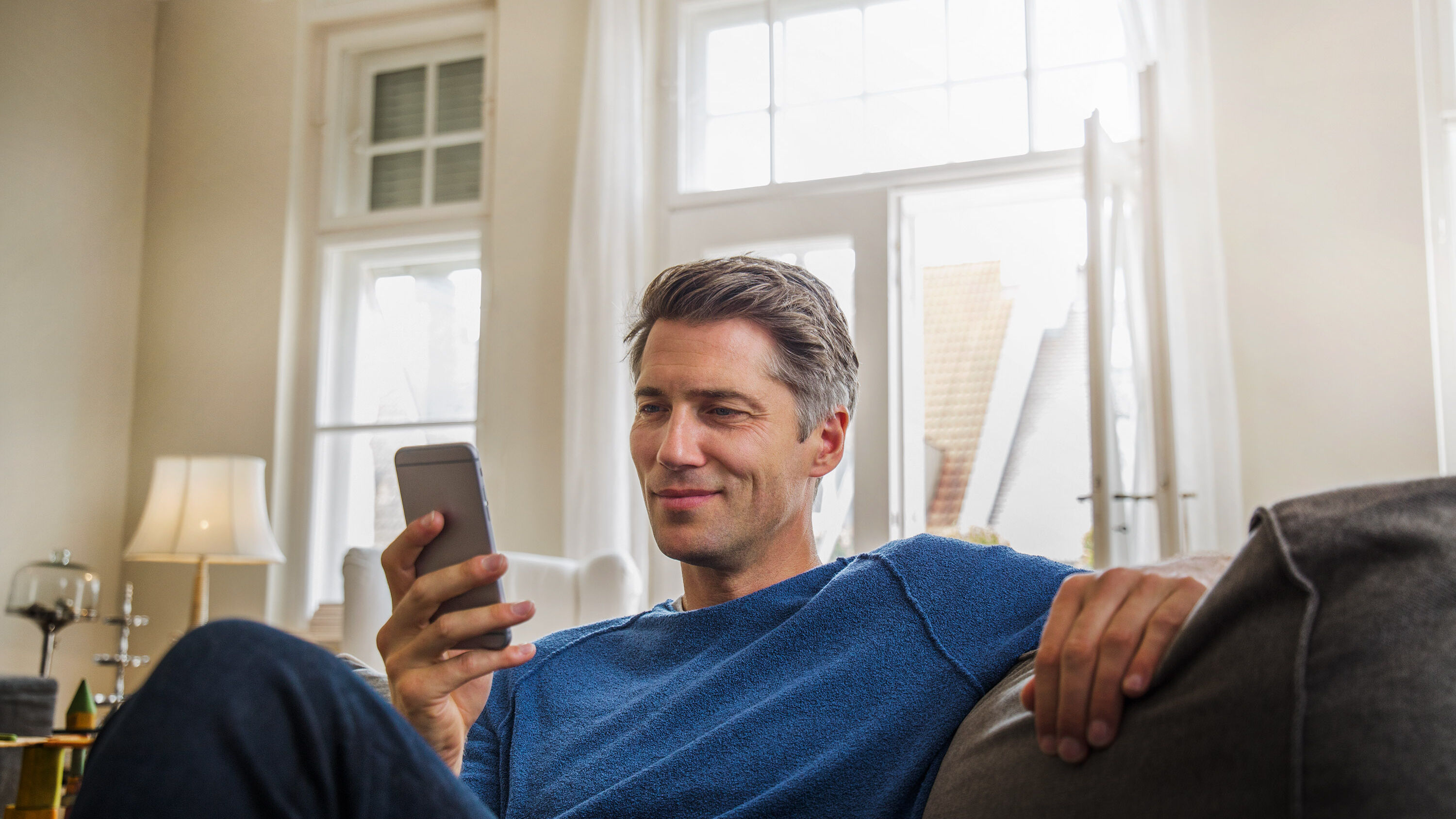 Ein Mann sitzt auf dem Sofa und blickt auf sein Handy