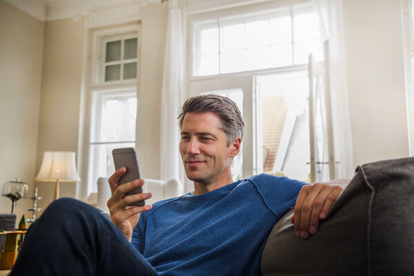 Ein Mann sitzt auf dem Sofa und blickt auf sein Handy
