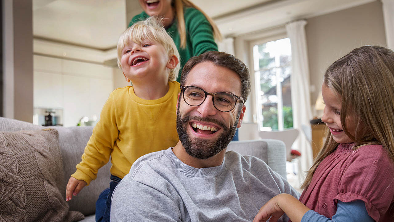 Eine Familie spielt gemeinsam im Wohnzimmer. Sie lachen fröhlich.