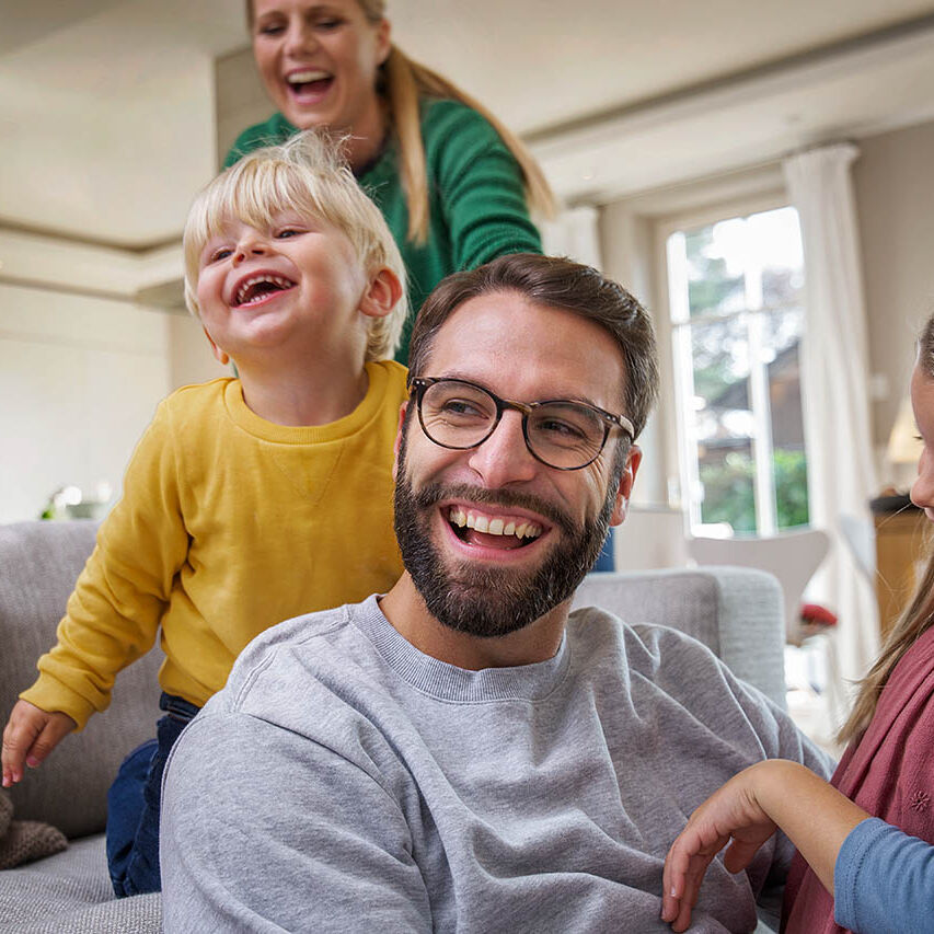 Eine Familie spielt gemeinsam im Wohnzimmer. Sie lachen fröhlich.