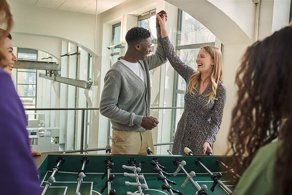 Mehrere junge Leute stehen um den Kickertisch herum, freuen sich und schlagen ihre Hände beieinander ein.