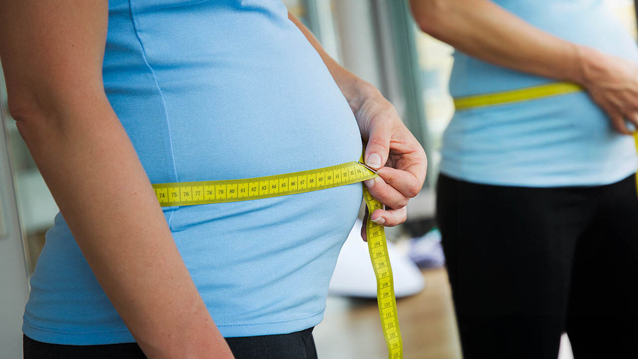 Eine schwangere Frau misst ihren Bauchumfang mit einem Maßband.