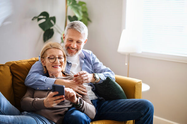 Glückliches älteres Ehepaar sitzt mit Handy auf der Couch