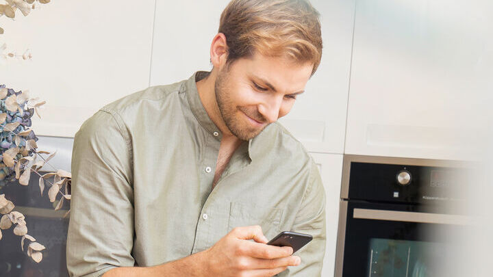 Ein Mann benutzt sein Mobiltelefon und lächelt dabei.