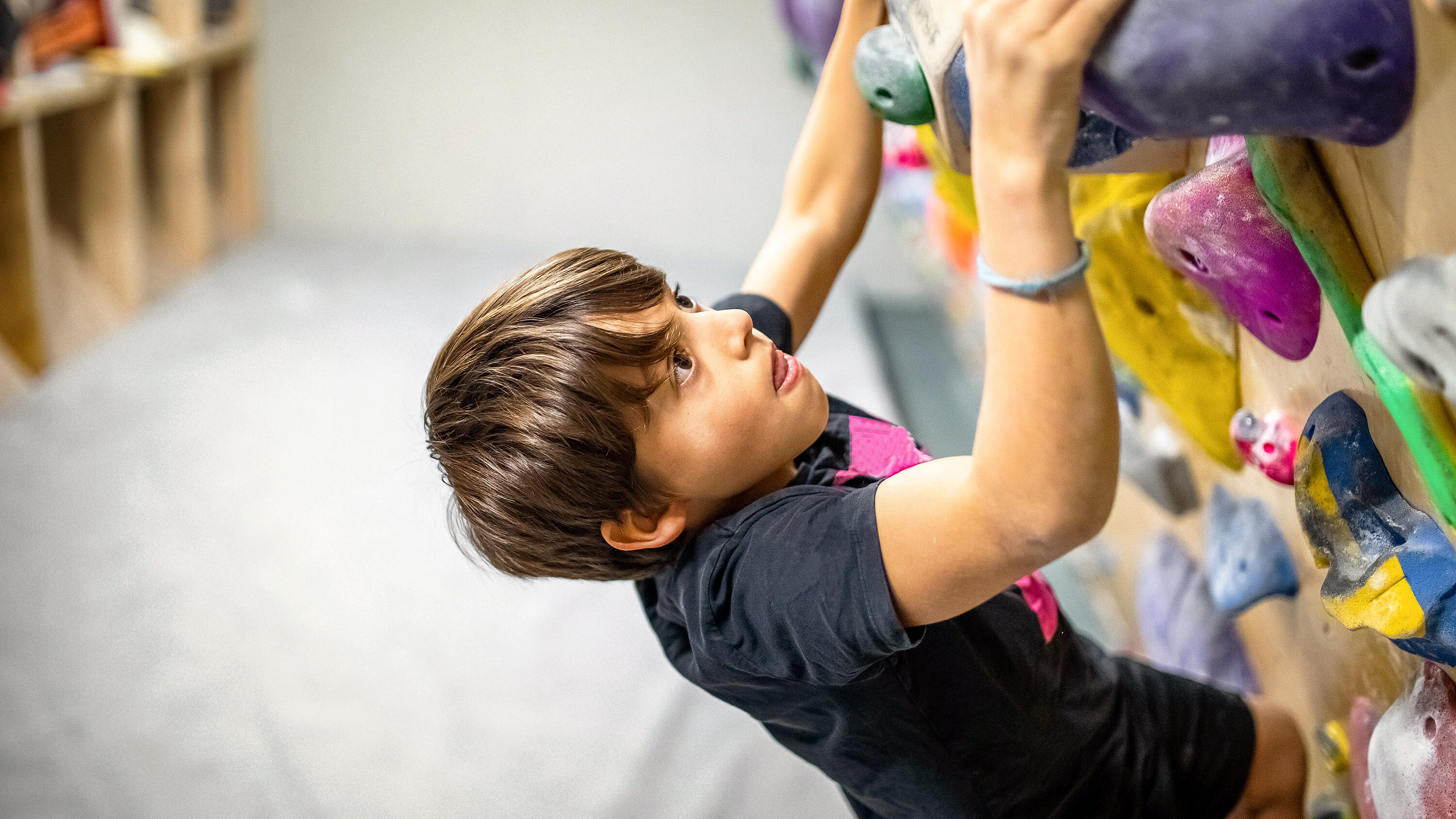 Ein Junge klettert an einer Boulderwand hoch und konzentriert sich.