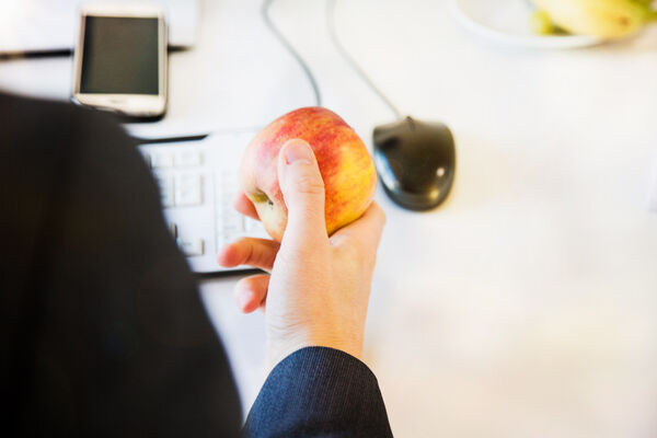 Rückenansicht eines Menschen am Arbeitsplatz mit Apfel in der Hand