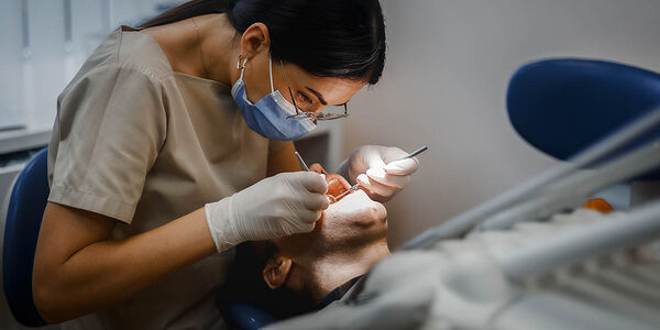 Eine Zahnarzthelferin kontrolliert die Zähne eines Patienten, der auf der Behandlungsliege liegt.