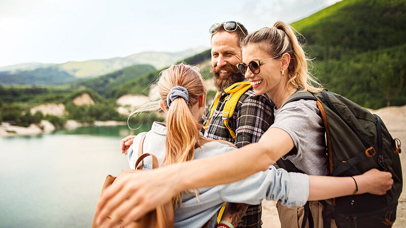 Eine Familie ist im Urlaub und umarmt sich glücklich an einem See.