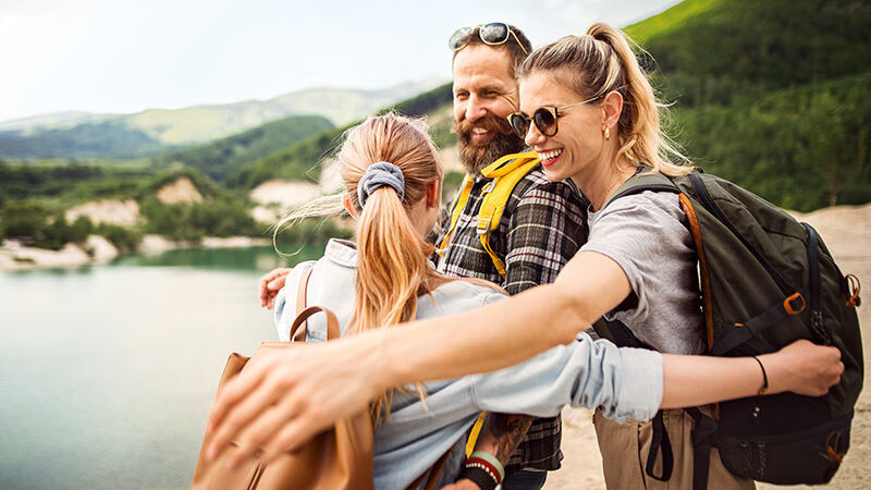 Eine Familie ist im Urlaub und umarmt sich glücklich an einem See.