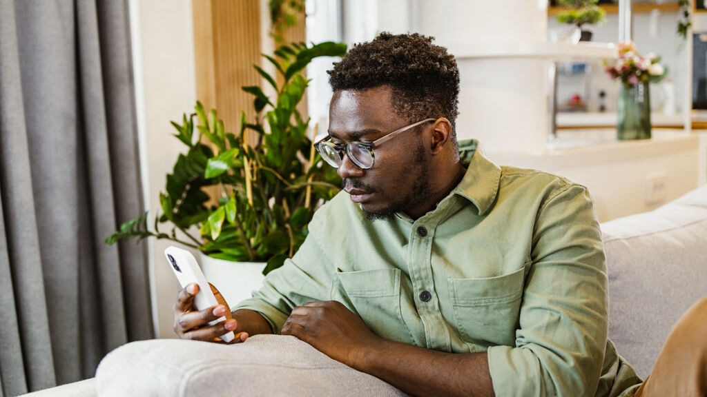 Ein Mann sitzt auf dem Sofa und benutzt sein Mobiltelefon.