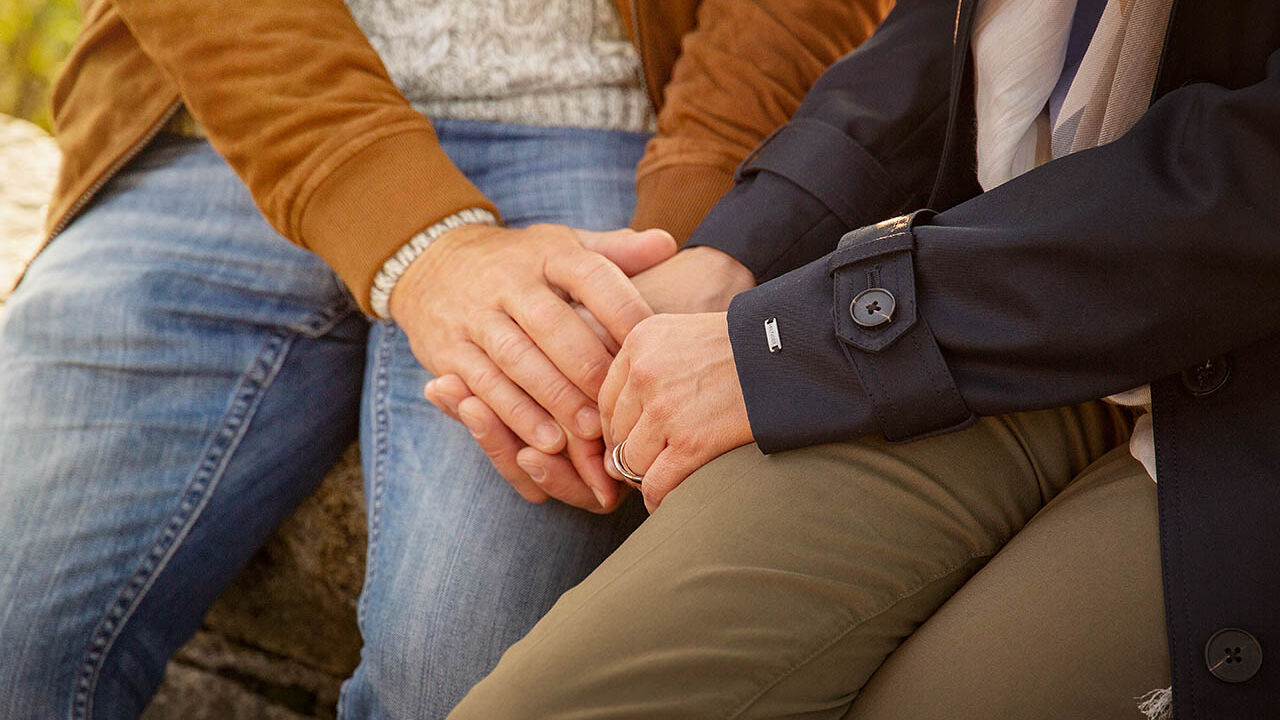 Ein Paar sitzt gemeinsam im Park und ein Mann hält die Hand seiner Partnerin.