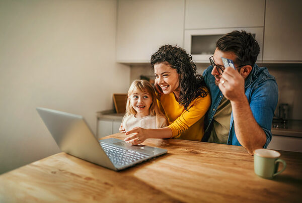 Eine Familie mit einem Kind interagieren in der Küche vor einem Laptop.