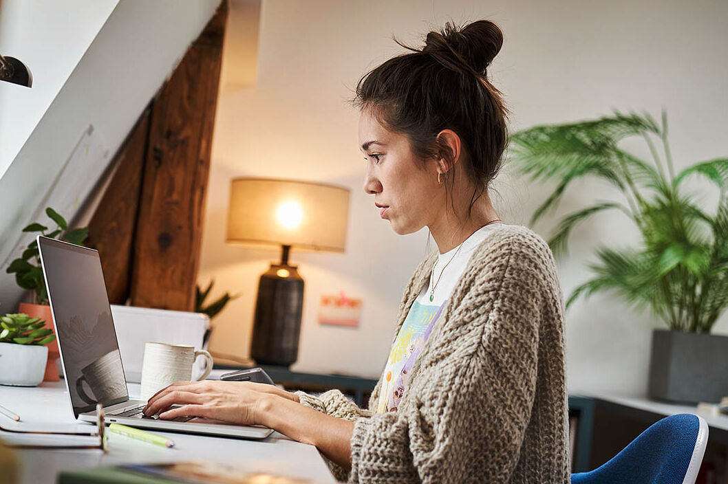 Eine Frau sitzt in ihrem Homeoffice und arbeitet an ihrem Laptop.