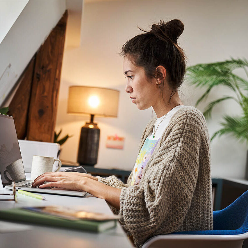 Eine Frau sitzt in ihrem Homeoffice und arbeitet an ihrem Laptop.