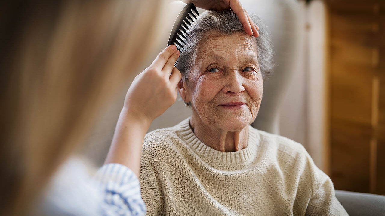 Einer älteren Frau werden ihre Haare von ihrer Enkelin gekämmt.  