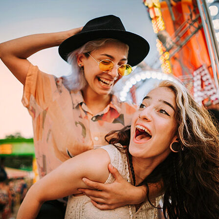 Zwei junge Frauen sind auf einem Festplatz und lachen miteinander.