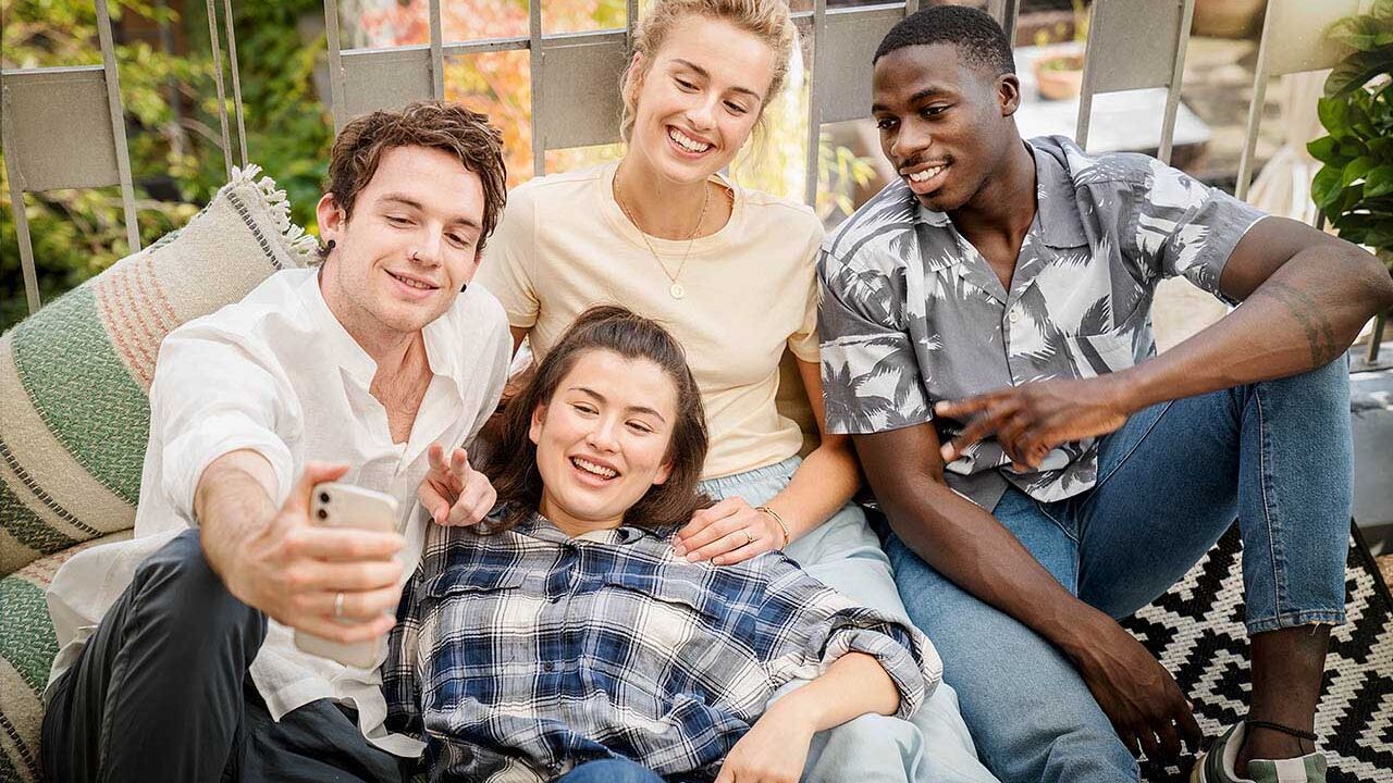 Eine Gruppe junger Erwachsener sitzt zusammen auf einem Balkon und macht ein Selfie zusammen.