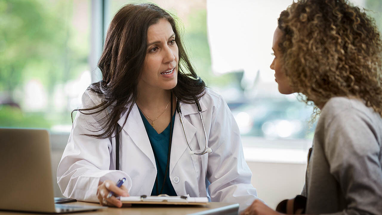 Eine Ärztin sitzt mit einer Patientin an einem Tisch und berät sie.