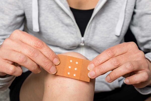 Wundheilung_GettyImages_1384285938_0925.jpg Eine Frau klebt ein Pflaster auf ihr verletztes Knie