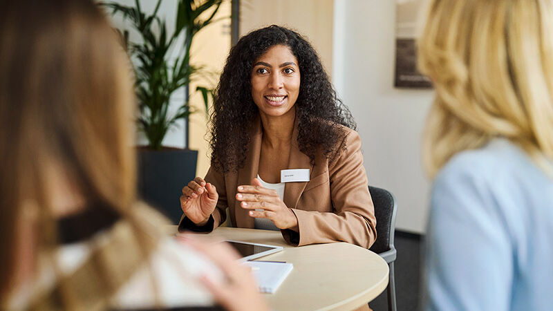 Eine Mitarbeiterin der SBK sitzt mit einer Kundin und ihrer Tochter an einem Tisch und berät sie.