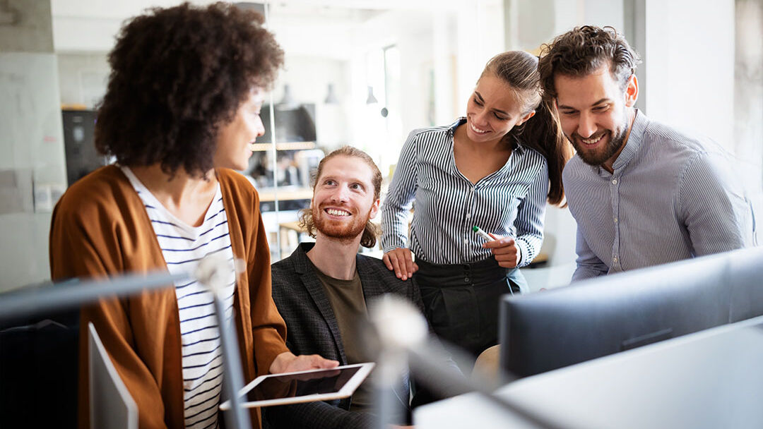 Junge Kolleginnen und Kollegen lachen zusammen am Arbeitsplatz