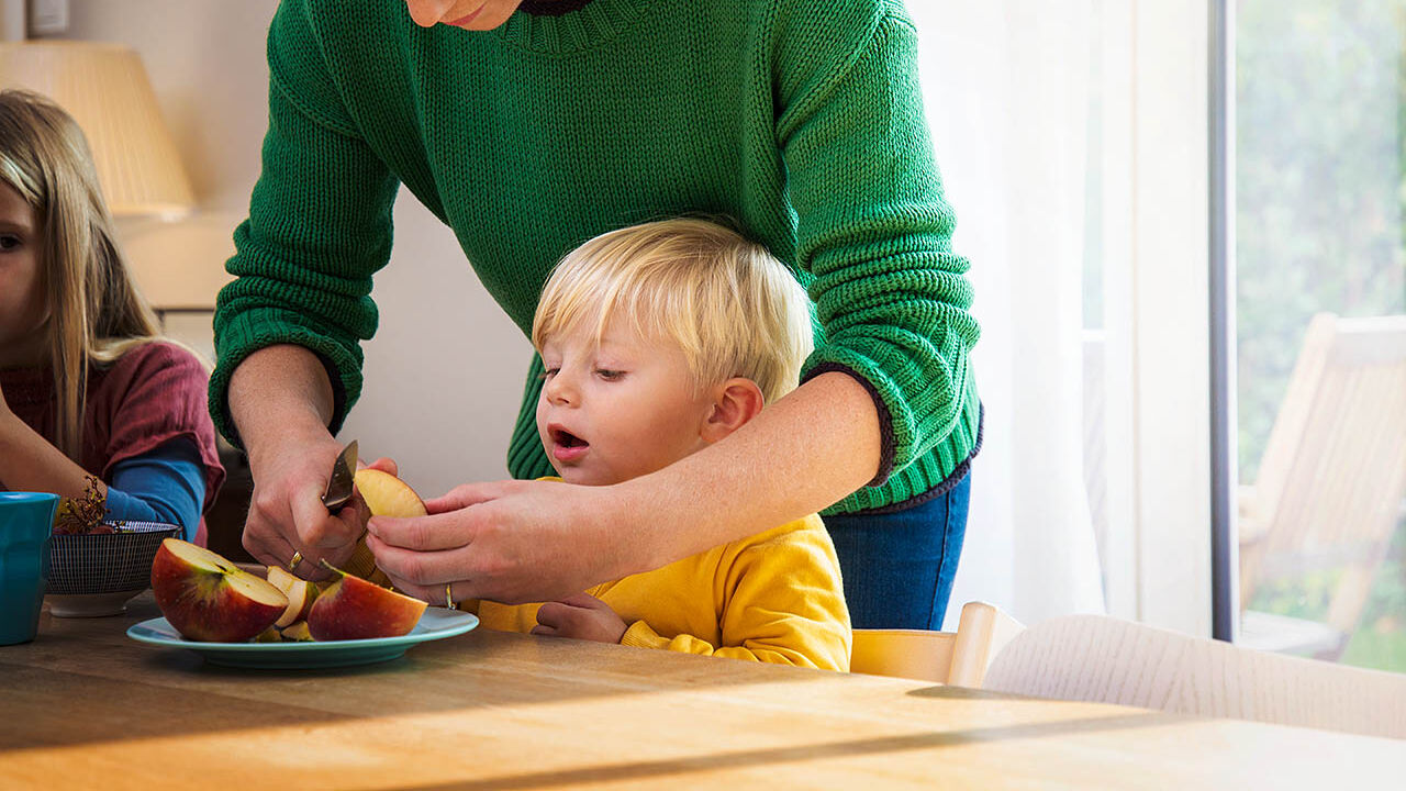 Eine Mutter schneidet einen frischen Apfel für ihren Sohn auf.