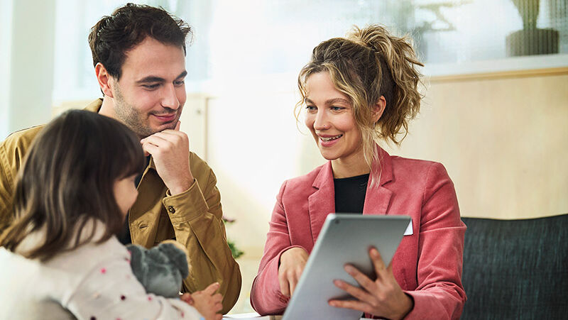 Eine Kundenberaterin berät einen Mann und seine kleine Tochter und zeigt ihnen etwas auf einem Tablet.