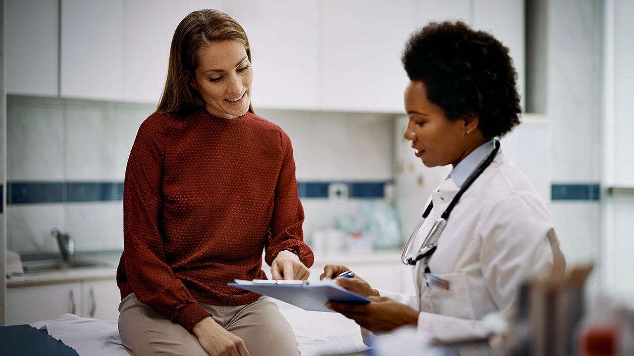 Eine Patientin sitzt auf einer Liege im Behandlungsraum und bespricht mit einer Ärztin ihre Behandlungsergebnisse.