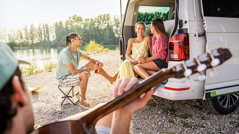 Junge Menschen sitzt vor einem Camping-Bus an einem See