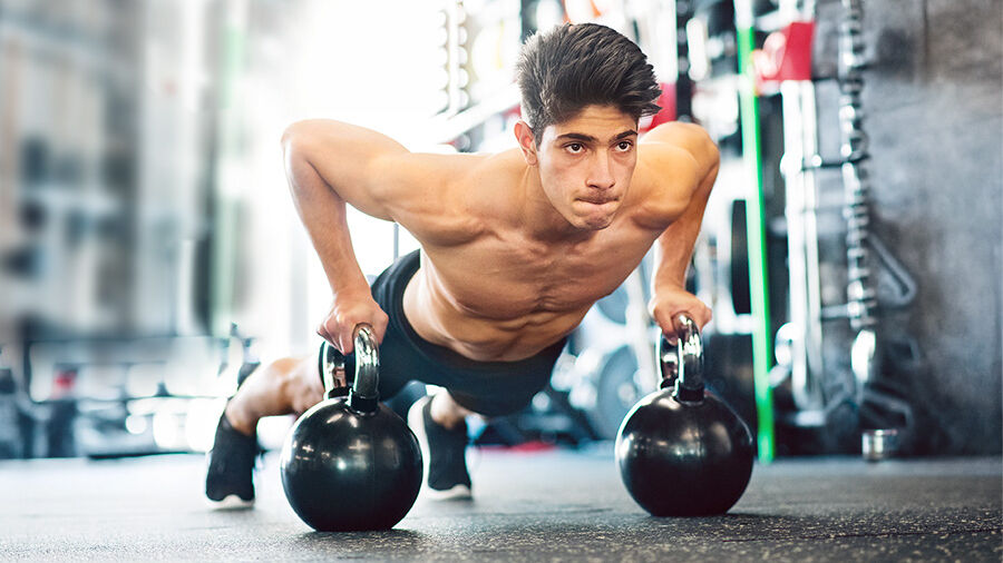 Junger Mann im Fitnessraum macht Push auf Kettleballs.