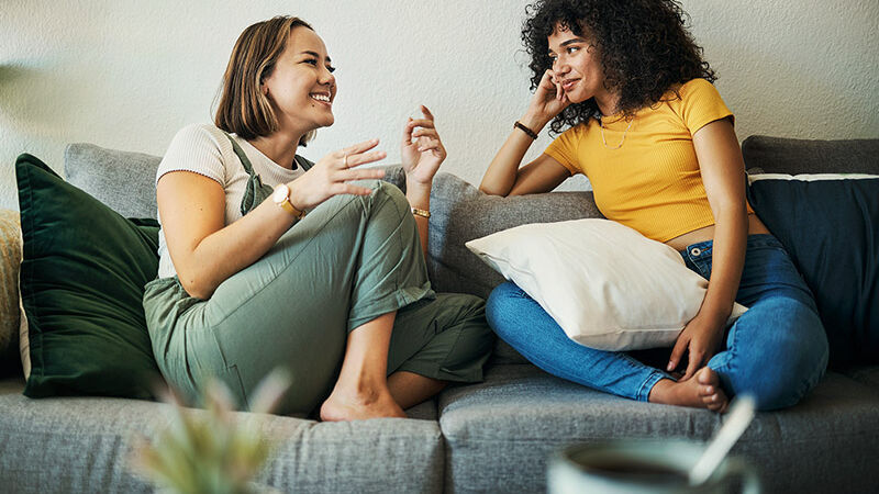 Zwei junge Frauen sitzen auf einem Sofa.