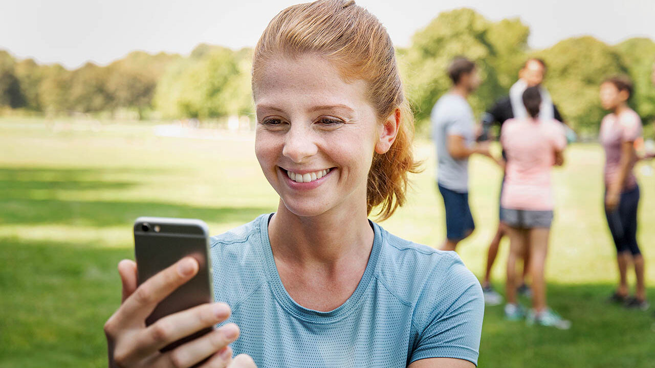 Eine Frau ist mit Freunden im Park und macht mit ihrem Handy einen Videoanruf.