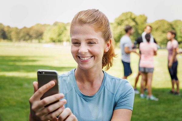 Eine Frau ist mit Freunden im Park und macht mit ihrem Handy einen Videoanruf. 