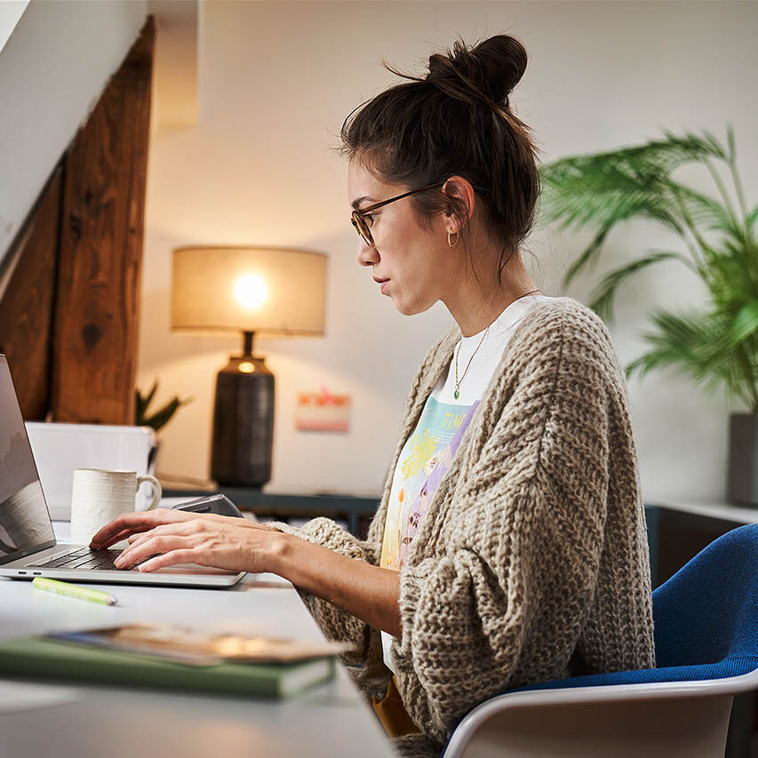 Eine Frau sitzt in ihrem Homeoffice und arbeitet an ihrem Laptop.