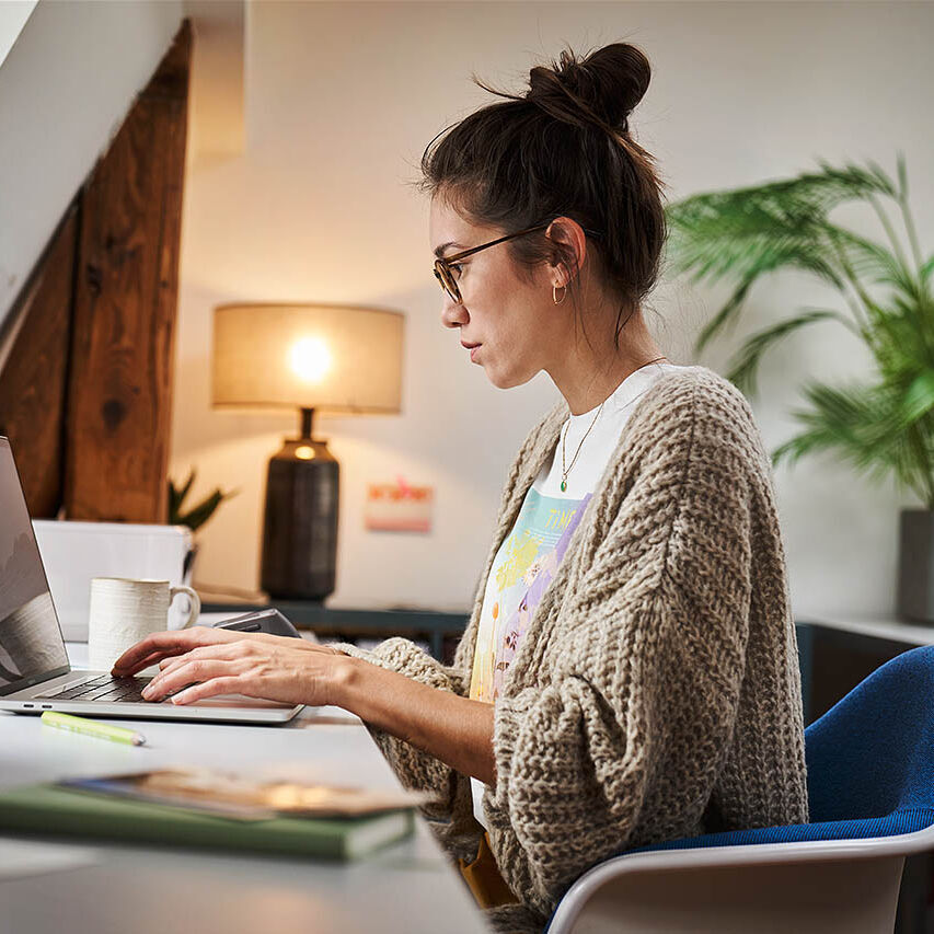 Eine Frau sitzt in ihrem Homeoffice und arbeitet an ihrem Laptop.