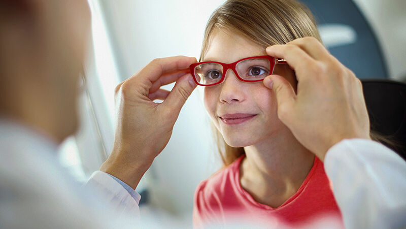 Ein Arzt kontrolliert die Brille eines Mädchens.