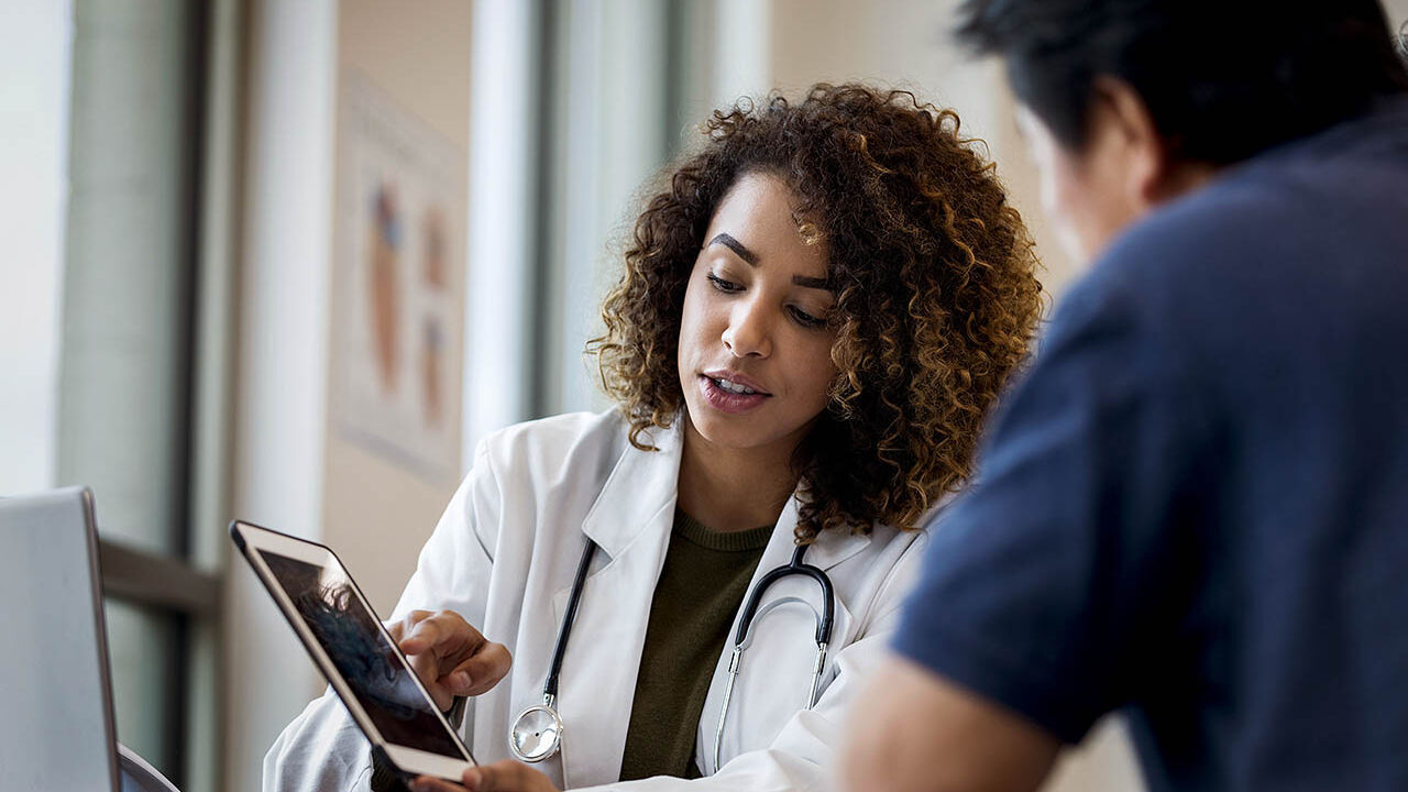 Eine Ärztin und ein Arzt besprechen sich anhand der Patientendaten auf einem Tablet.