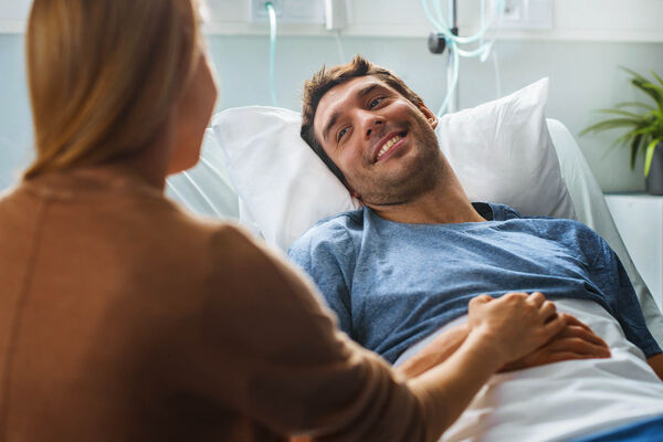 Ein junger Mann liegt im Bett im Krankenhaus und hat Besuch von seiner Freundin.