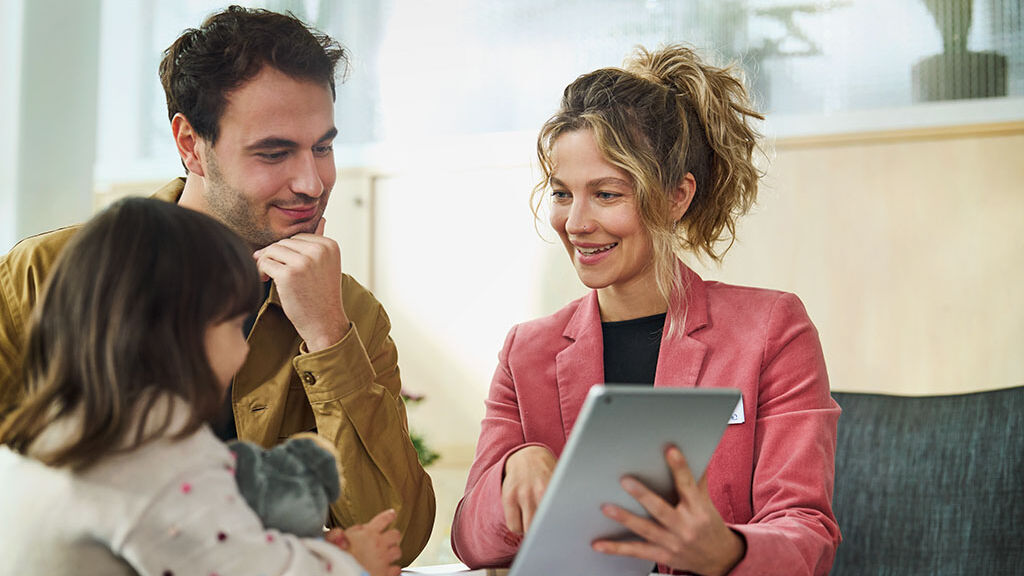 Eine Kundenberaterin berät einen Mann und seine kleine Tochter und zeigt ihnen etwas auf einem Tablet.