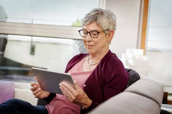 Ältere Frau sitzt mit Tablet auf dem Sofa