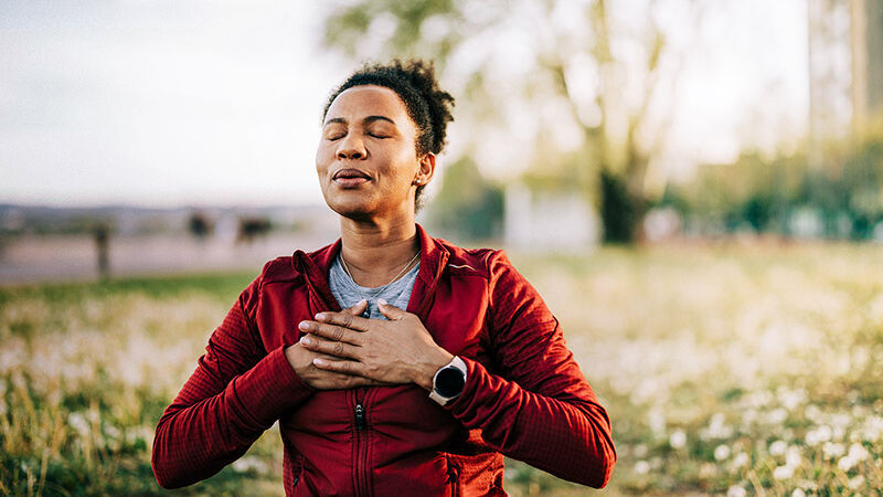 Eine Frau sitzt in der Natur und macht Entspannungsübungen.