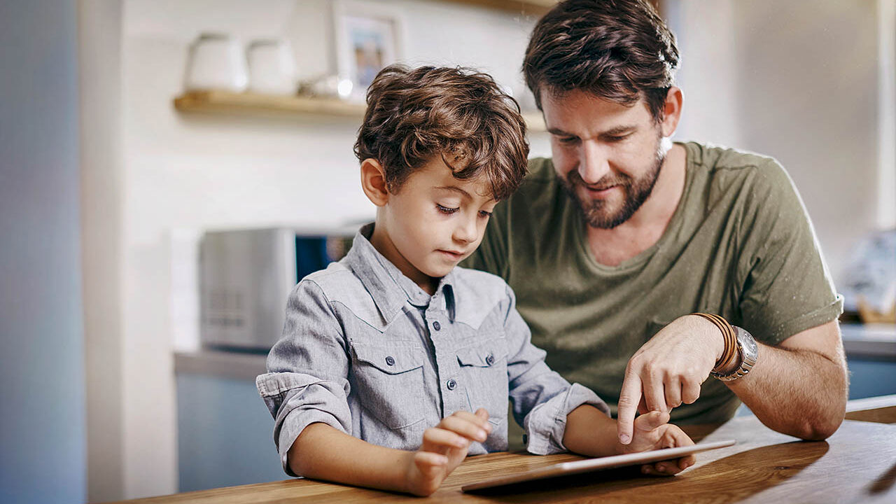 Ein Vater übt mit seinem Sohn die Benutzung des Tablets.