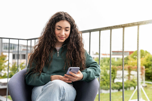 Ein Mädchen sitzt auf dem Balkon und schaut in ihr Handy.