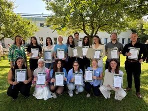 Gruppe Auszubildende unter Bäumen hält Urkunden für Baumspende hoch