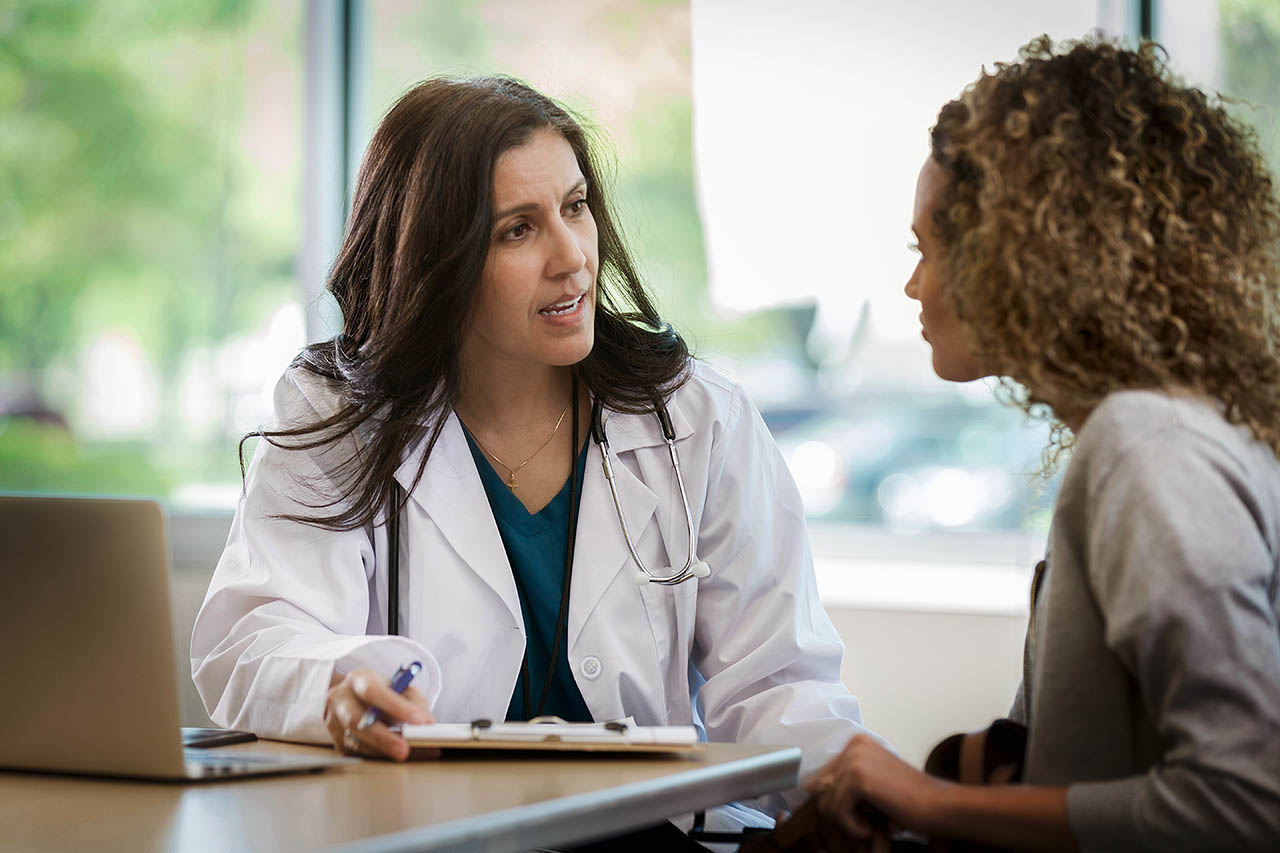 Eine Ärztin sitzt mit einer Patientin an einem Tisch und berät sie.