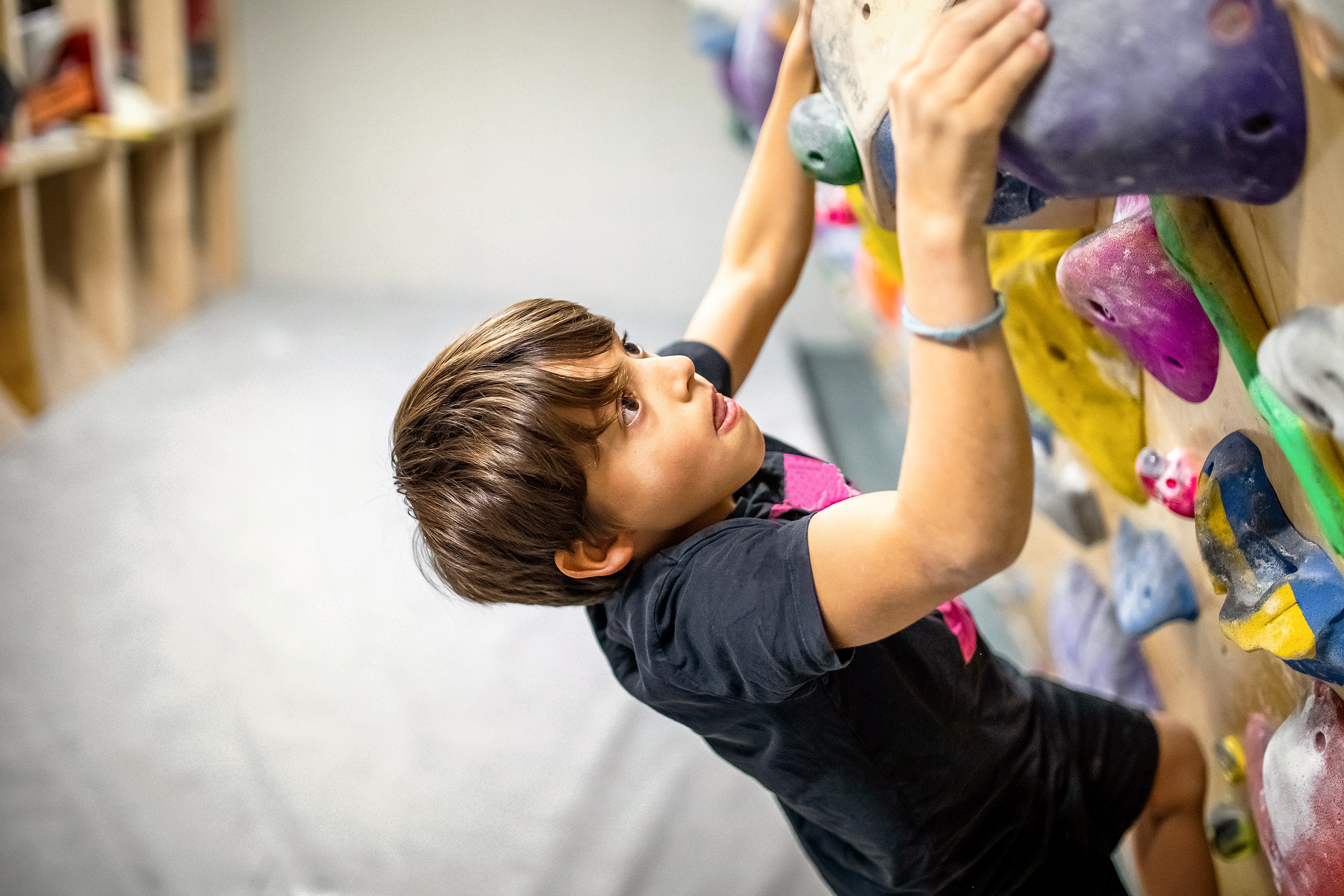 Ein Junge klettert an einer Boulderwand hoch und konzentriert sich.