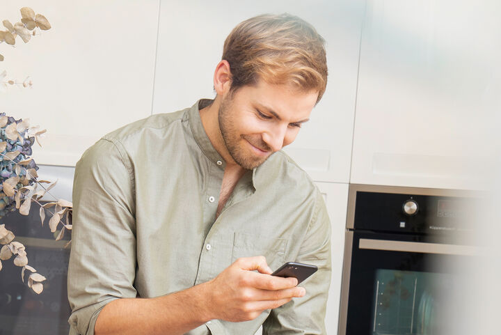 Ein Mann benutzt sein Mobiltelefon und lächelt dabei.