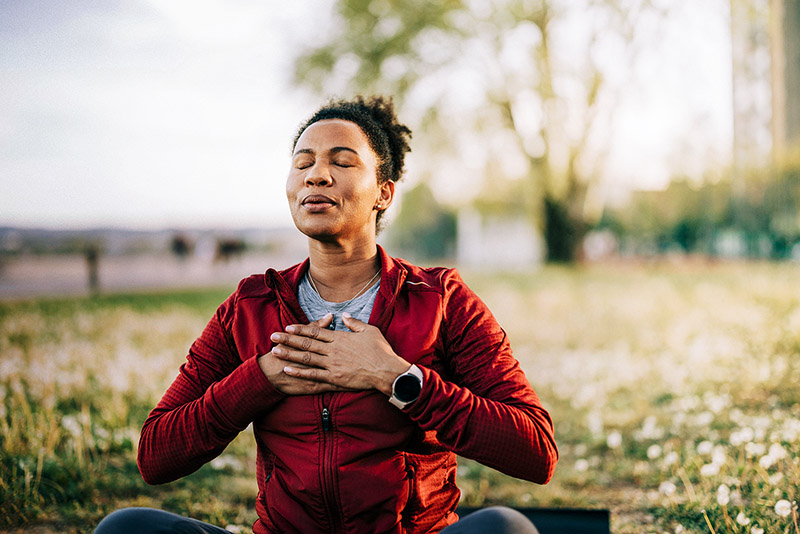 Eine Frau sitzt in der Natur und macht Entspannungsübungen.