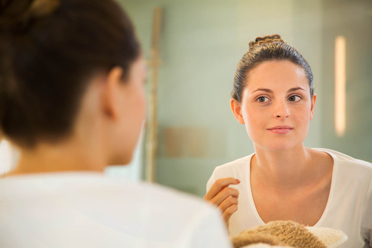 Eine junge Frau betrachtet sich selbst im Spiegel.